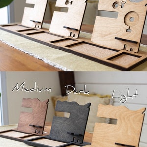 May include: Three wooden phone stands with different features. The stand on the left has no extra features, the middle stand has a watch holder, and the stand on the right has a watch holder and a MagSafe charger. The bottom row shows three different wood finishes: medium, dark, and light.