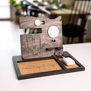 May include: A wooden phone stand with a cork base. The stand has two charging pads, a watch holder, and a slot for a phone. The stand is personalized with the initials "B.W." and the name "Oscar Edgardo Lagos".