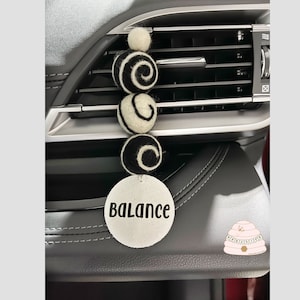 May include: A white and black car air freshener with a round, white tag that says "Balance". The air freshener is made of felt and has a spiral design.