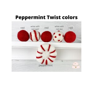 May include: A garland of felt balls in red, white with red swirl, white with red dots, and peppermint colors. The garland is strung on a white string and is hanging from a white shelf. The text "Peppermint Twist colors" is written above the garland.