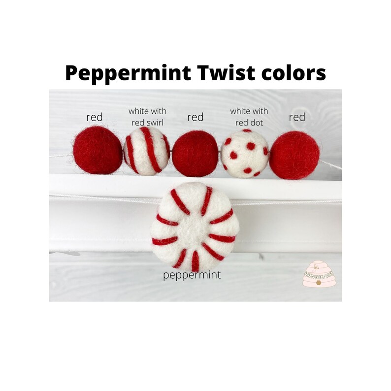 May include: A garland of felt balls in red, white with red swirl, white with red dots, and peppermint colors. The garland is strung on a white string and is hanging from a white shelf. The text "Peppermint Twist colors" is written above the garland.