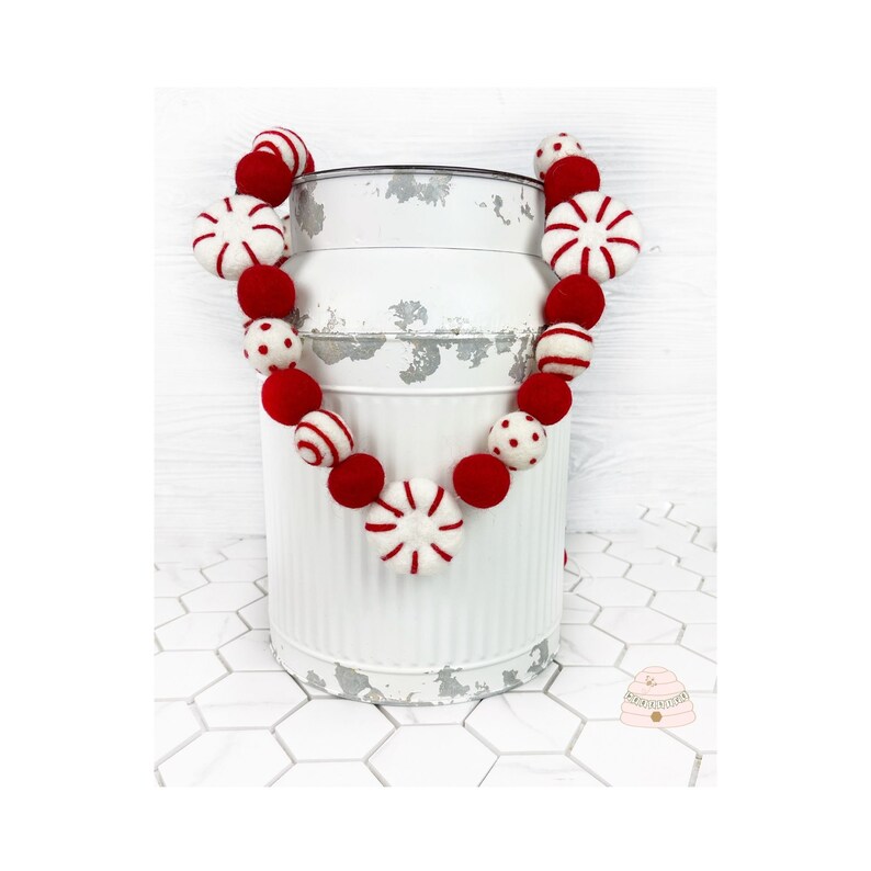 May include: A red and white felt garland with peppermint candy designs. The garland is draped over a white milk can.
