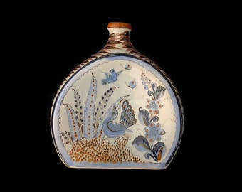Könnte beinhalten: Eine dekorative Keramikflasche mit flachem, rundem Körper und schmalem Hals. Die Flasche zeigt ein handgemaltes Design eines Vogels, Blumen und Blättern in Blau-, Braun- und Weißtönen. Der Rand und der Hals sind mit braunen und weißen Mustern verziert.