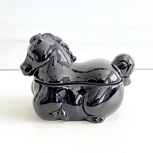 May include: A black ceramic piggy bank shaped like a horse. The piggy bank has a glossy finish and a small opening on the back for inserting coins.