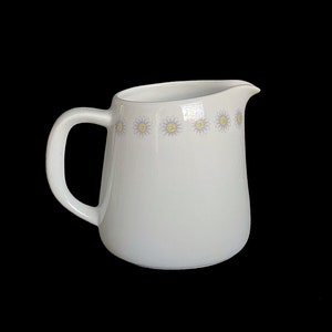 May include: White ceramic creamer with a band of purple and yellow daisies around the middle.