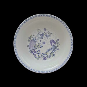 May include: A white ceramic bowl with a blue and purple floral design featuring two figures. The bowl has a blue and white border.