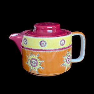 May include: A ceramic teapot with a red lid and a yellow, orange, and red design. The teapot has a white handle and a stylized sun design.