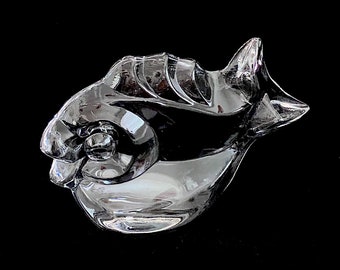 May include: A clear glass sculpture of a fish with a detailed, textured design. The fish is facing to the right and has a slightly curved body.