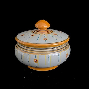 May include: A ceramic lidded jar with a white base and orange and green accents. The jar has a round shape and a lid with a knob on top.