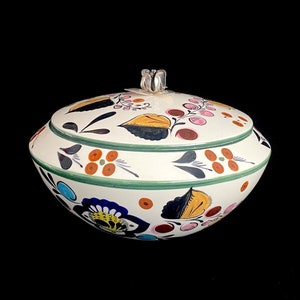 May include: A white ceramic lidded bowl with a floral design. The bowl features a green rim and is decorated with colorful flowers, leaves, and berries in shades of blue, yellow, orange, and pink. The lid has a silver-colored handle.