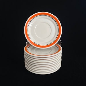 May include: A stack of 12 white ceramic saucers with a thin orange and black trim around the edge.