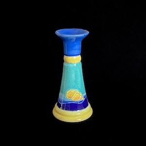 May include: A blue and yellow ceramic candle holder with a seashell design. The holder has a wide base and a narrow top.