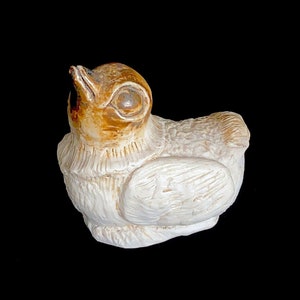 May include: A small, white ceramic bird figurine with brown accents. The bird has its head tilted up and its beak open, as if it is singing.
