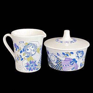 May include: A white ceramic creamer and sugar bowl set with a blue and green floral pattern. The pattern features stylized figures of people.