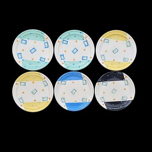 May include: Six decorative ceramic plates with different color and geometric patterns. Each plate features a white background with blue, yellow, and black accents. The plates are decorated with small squares and dots.