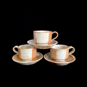 May include: Three brown and white ceramic teacups and saucers. The cups and saucers have a mottled glaze.