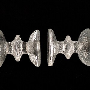 May include: Two clear glass candle holders with a textured surface and a unique, modern design.