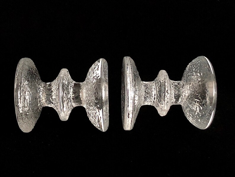 May include: Two clear glass candle holders with a textured surface and a unique, modern design.
