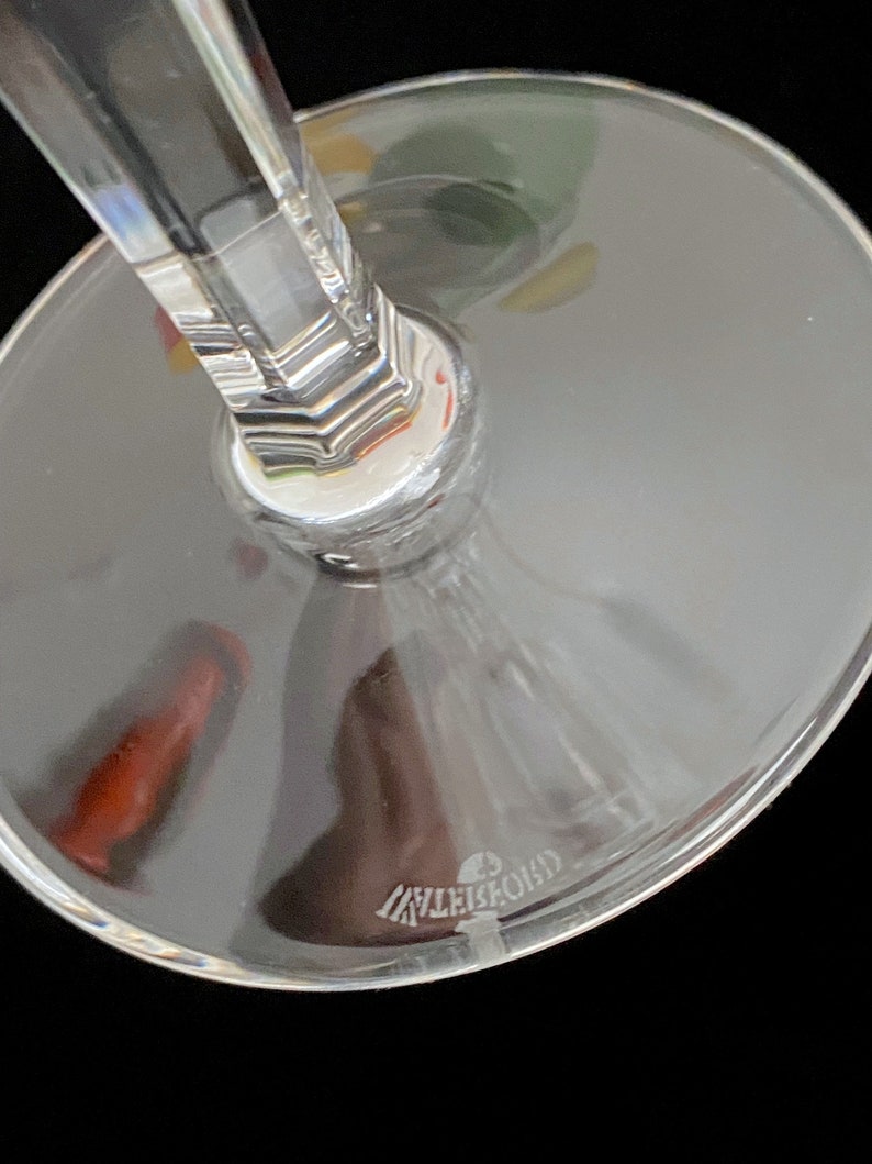 K&ouml;nnte beinhalten: Nahaufnahme des Bodens eines klaren Weinglases aus Glas mit einem dicken Stiel. Das Glas hat einen klaren, runden Boden mit dem Wort "Lalique" in den Boden ge&auml;tzt.