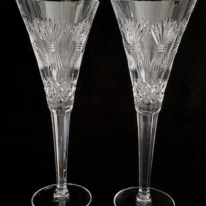 K&ouml;nnte beinhalten: Zwei klare Champagnerfl&ouml;ten aus Glas mit geschliffenem Kristallmuster. Die Fl&ouml;ten haben einen hohen, schlanken Stiel und eine breite, schalenf&ouml;rmige Oberseite.