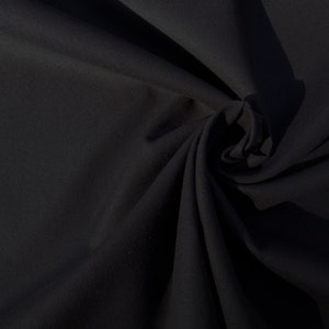 May include: A close-up of a black fabric with a smooth texture. The fabric is folded and draped, creating soft folds and curves.