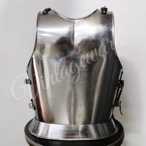 K&ouml;nnte beinhalten: Ein polierter, silberfarbener Brustpanzer mit abgerundeter Basis und gebogenem Oberrand. Die R&uuml;stung hat Riemen und Schnallen zum Befestigen. Die Oberfl&auml;che reflektiert das Licht und hebt die glatte, metallische Oberfl&auml;che hervor. Der Brustpanzer ist ein historisches R&uuml;stungsteil.