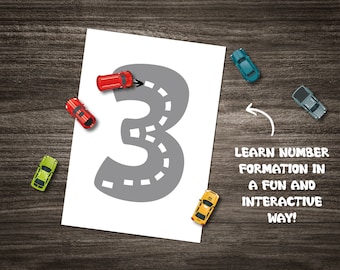 May include: A white sheet of paper with a gray number three drawn on it. The number three is shaped like a road with dashed lines. There are five toy cars of different colors driving on the road. The text "LEARN NUMBER FORMATION IN A FUN AND INTERACTIVE WAY!" is written below the number.
