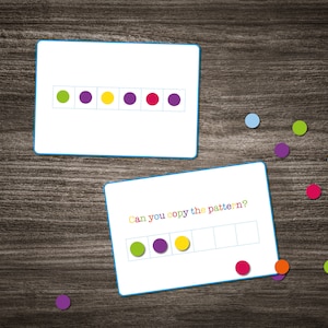 Może przedstawiać: Gra edukacyjna z dwoma kartami. Górna karta przedstawia wzór z zielonych, fioletowych, żółtych, fioletowych, czerwonych i fioletowych kółek. Dolna karta ma ten sam wzór rozpoczęty, ale z pustymi miejscami do wypełnienia. Tekst na dolnej karcie brzmi "Czy potrafisz skopiować wzór?"