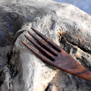 May include: A dark brown wooden fork with four tines, resting on a piece of weathered driftwood.