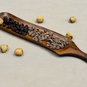 May include: A long, wooden serving tray with a handle. The tray is filled with dried cranberries and candied nuts.