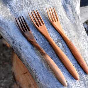 May include: Three wooden forks with different wood grain patterns. The forks are laid out on a piece of weathered wood.