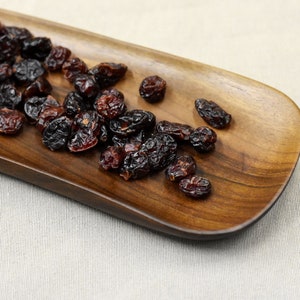 May include: A wooden serving dish with a pile of dried cranberries on it.