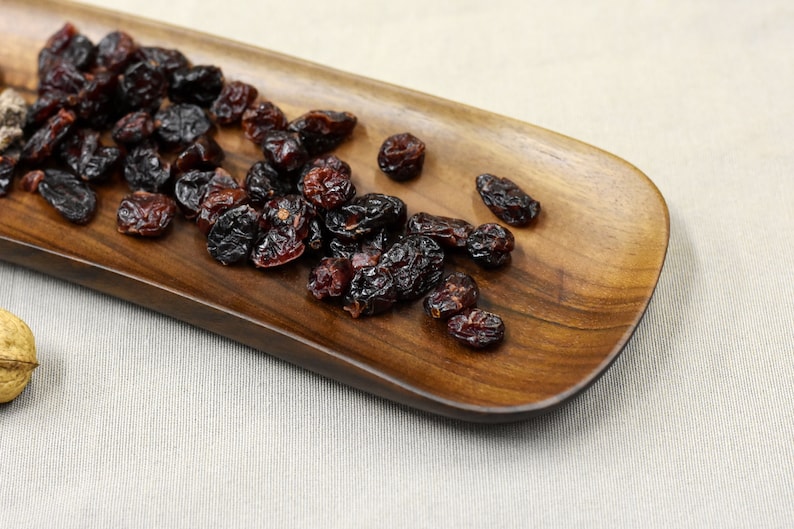 May include: A wooden serving dish with a pile of dried cranberries on it.