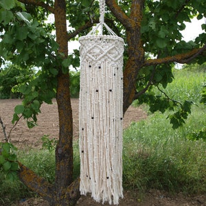 May include: A white macrame hanging lamp with black beads. The lamp is hanging from a tree branch.