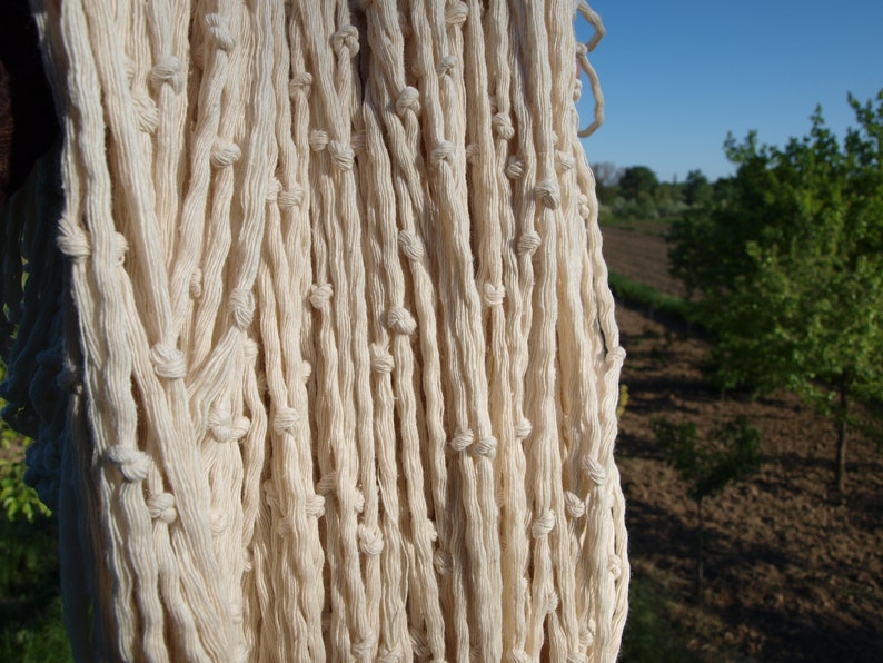 May include: Close-up of a white cotton rope hanging in a field. The rope is woven in a tight pattern and has a natural, rustic look.