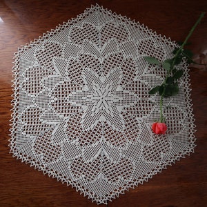 以下が含まれることがあります： 繊細な花柄の白いクロシェのドイリーで、上に赤いバラが1輪置かれています。