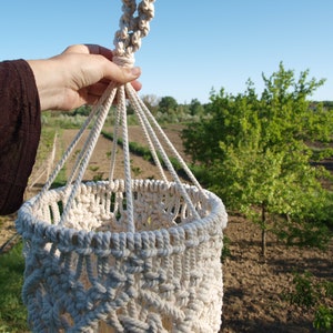May include: A white macrame plant hanger with a round base and a knotted top. The hanger is made of thick cotton rope and has a delicate pattern.