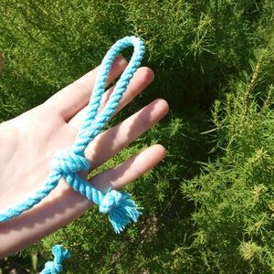 May include: A hand holding a light blue rope tied in a knot. The rope is made of a soft, woven material.