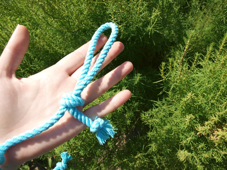 May include: A hand holding a light blue rope tied in a knot. The rope is made of a soft, woven material.