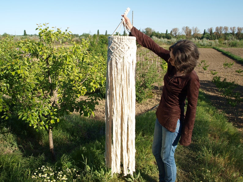 May include: A white macrame wall hanging with a fringe design. The hanging is made of natural fibers and has a rustic, bohemian style.