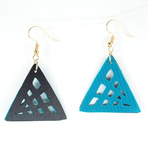 Op de afbeelding: Een paar driehoekige oorbellen. Eén is zwart met uitgesneden geometrische vormen, de andere is turquoise met een streepjespatroon en uitgesneden vormen. Beide hebben goudkleurige oorhaken.