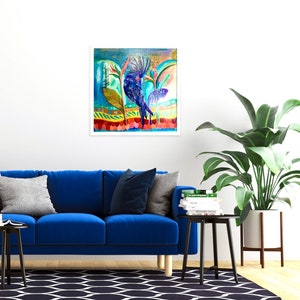 May include: A framed watercolour painting of a stylized blue bird in a colourful, tropical setting. The artwork, with a white border, hangs above a blue sofa. The painting's vibrant colours include blues, greens, and reds, creating a tropical theme.