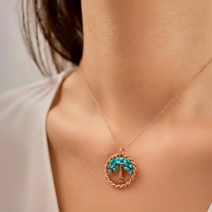 Puede incluir: Un collar de oro rosa con un colgante con forma de árbol. Las hojas del árbol están hechas de pequeñas piedras de color turquesa. El colgante está rodeado por un diseño de cuerda trenzada, y la cadena es delicada.