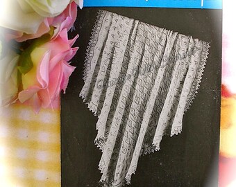May include: A vintage baby shawl pattern designed by Penelope, shown against a black backdrop. The shawl is white with a detailed lace pattern. The text "W.B. Baby Wool" is visible. Pink and white roses are in the background.