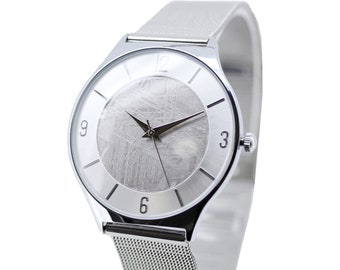 May include: A silver wristwatch with a mesh band and a round face. The watch face features a textured, gray design, with black hands and silver hour markers at 3, 6, 9, and 12. The watch is displayed against a white background.