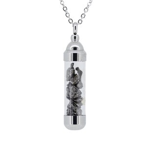 May include: A silver chain necklace with a clear glass tube pendant containing small pieces of dark grey meteorite. The pendant has a silver cap on each end.