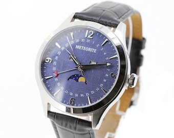 May include: A silver watch with a blue face and black leather band. The watch face has a calendar, moon phase, and the word "METEORITE" printed on it.