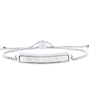 Może przedstawiać: Srebrna bransoletka z białą, fakturowaną zawieszką w kształcie prostokąta. Bransoletka ma regulowany, przesuwany zamek.