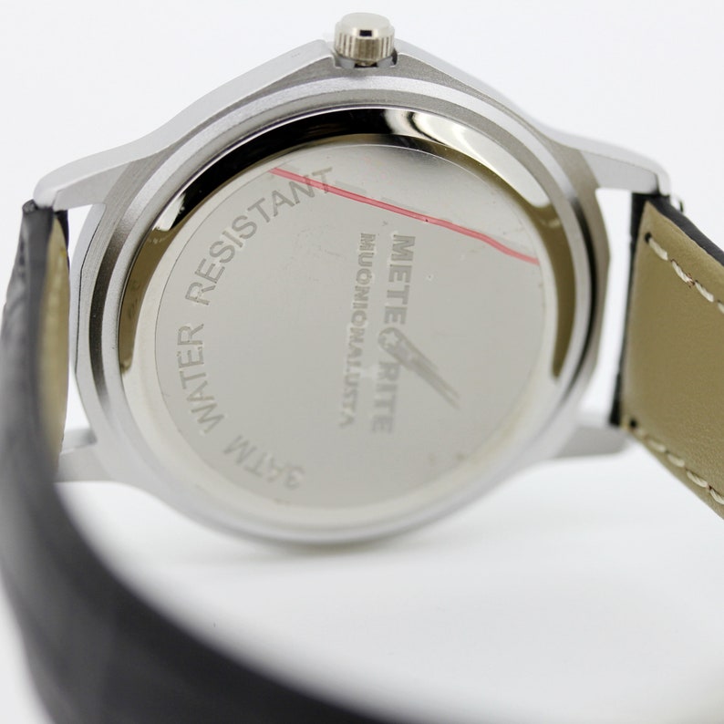 Pode incluir: A parte de tr&aacute;s de um rel&oacute;gio prateado com uma pulseira de couro preto. O mostrador do rel&oacute;gio diz "METEORITE" e "WATER RESISTANT 3ATM".