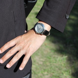 Pode incluir: Um rel&oacute;gio de pulso prateado com uma pulseira de couro preta. O mostrador do rel&oacute;gio tem um fundo branco com marcas pretas.